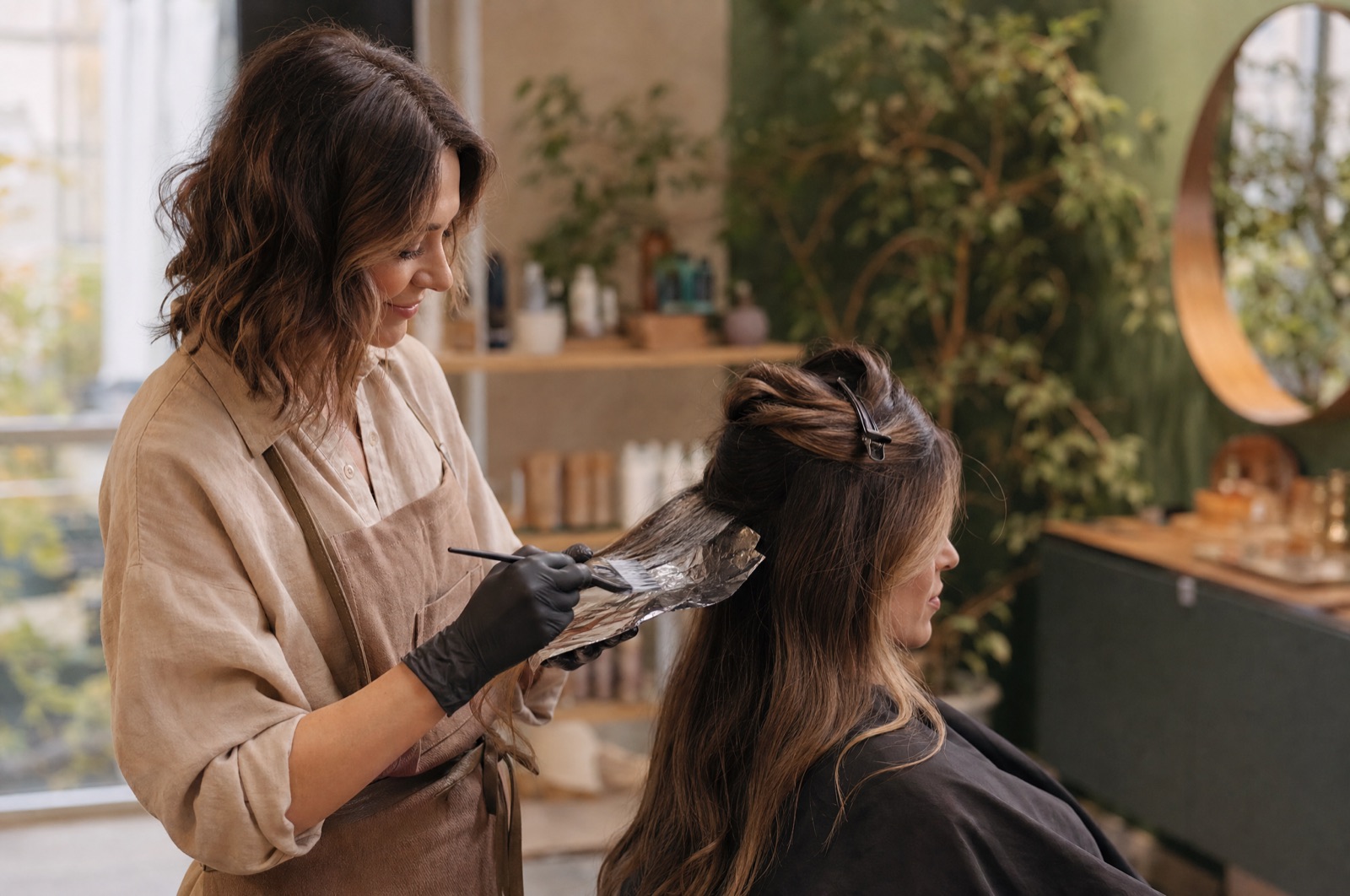 Friseurin trägt Balayage-Farbe auf. Mit KI gestaltet.